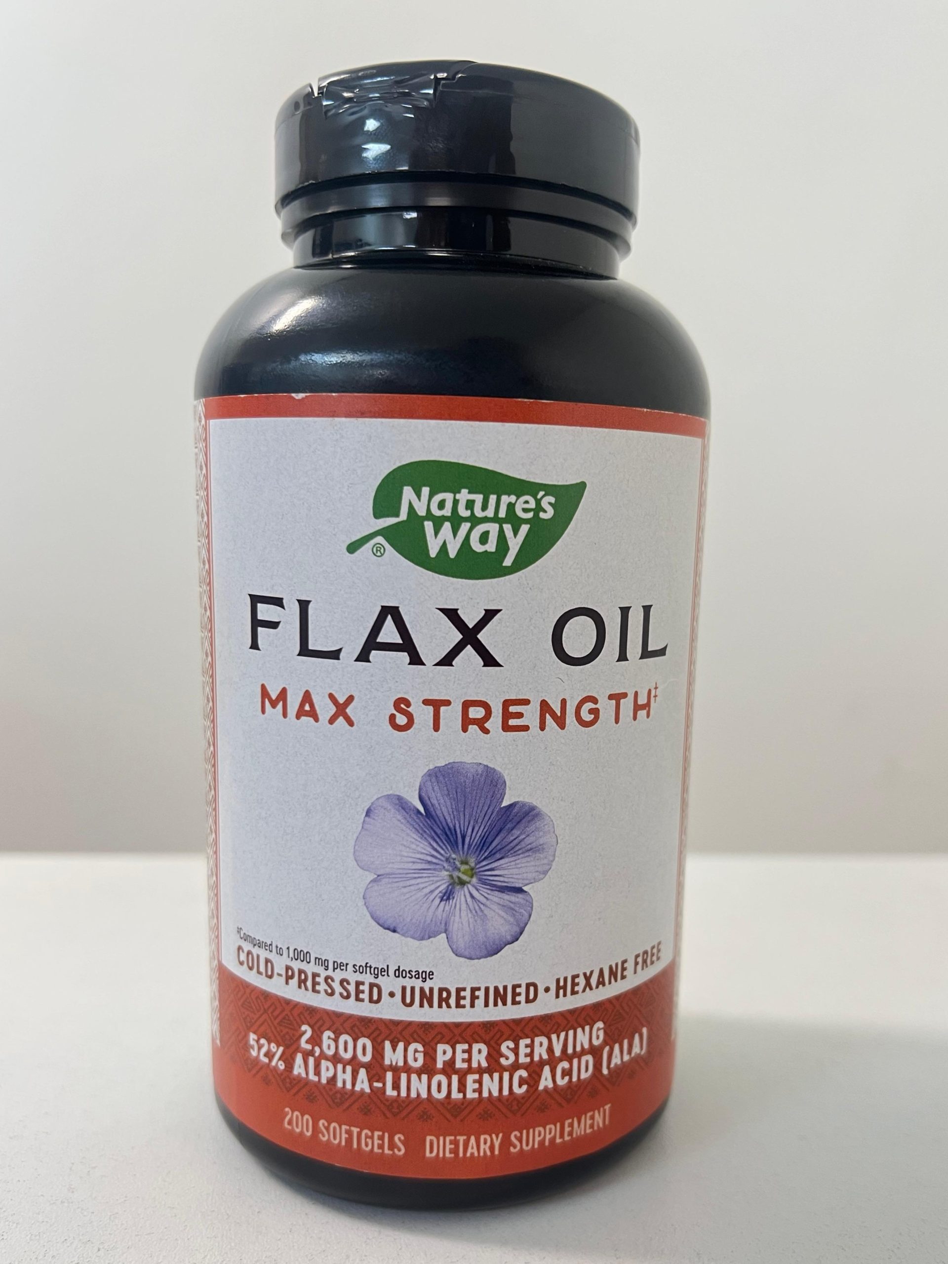 Front of Nature’s Way Flax Oil Max Strength bottle. Black bottle with white and orange label featuring a purple flax flower. Highlights cold-pressed, unrefined, hexane-free formula with 2,600 mg per serving and 52% ALA. Contains 200 softgels.